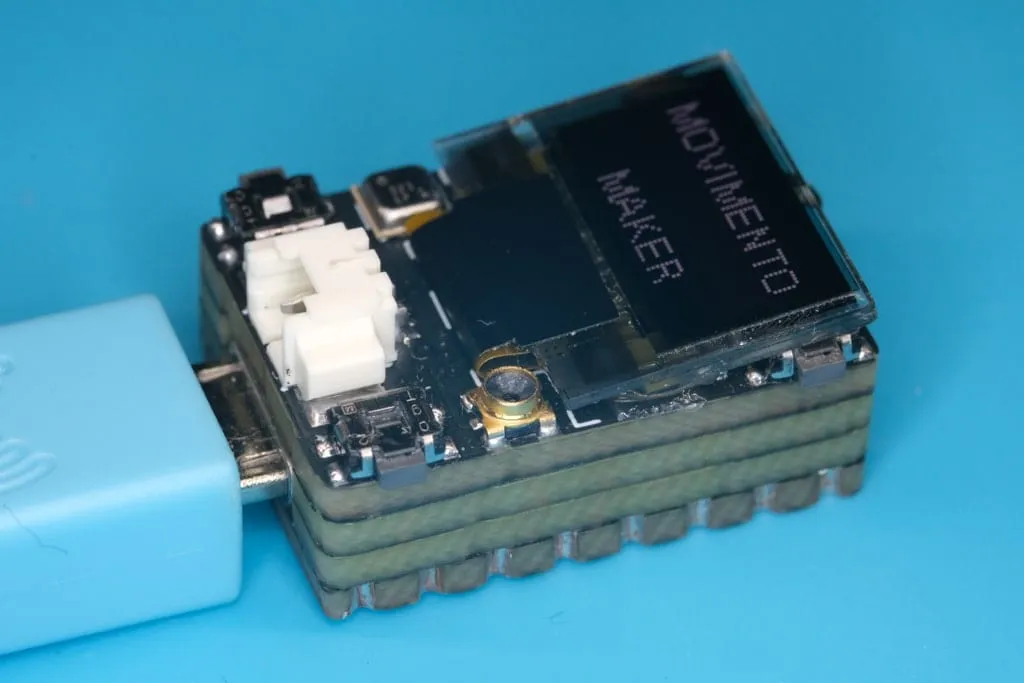 World's Smallest ESP32 V2 board with its OLED screen, plugged into a USB cable