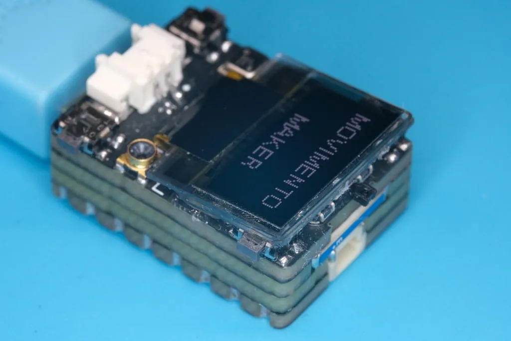 V2 plugged into USB, OLED showing “Movimento Maker”